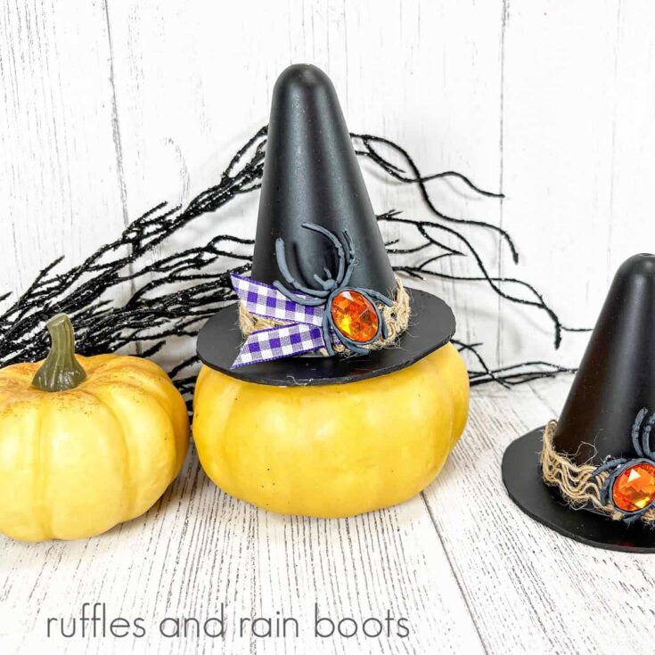 Two yellow gourds, one with a witch's hat on it and another witch's hat against a white weathered wood background.