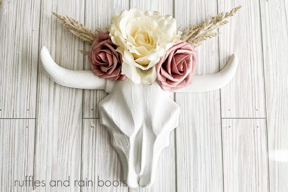 A close up of a decorated plastic skull against a white weathered wood background.