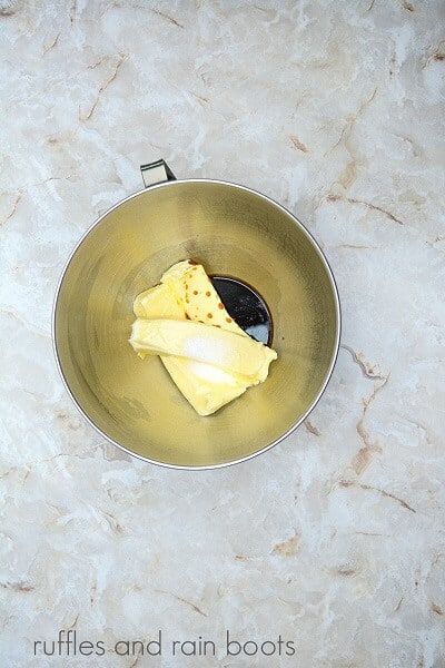 A large metal mixing bowl filled with butter, salt and vanilla against a marble surface.