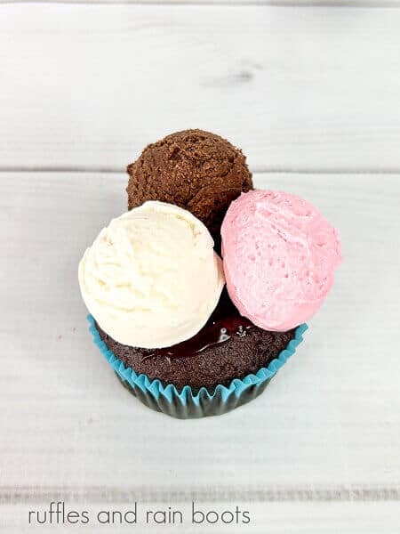 3 scoops of frosting on top of a chocolate cupcakes against a white weathered wood background.