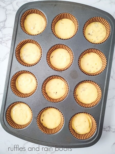 Butterfinger cupcake batter in a 12 cavity metal pan on a white marble surface.