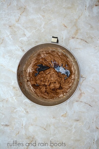 A large metal mixing bowl filled cupcake batter and coffee against a marble surface.