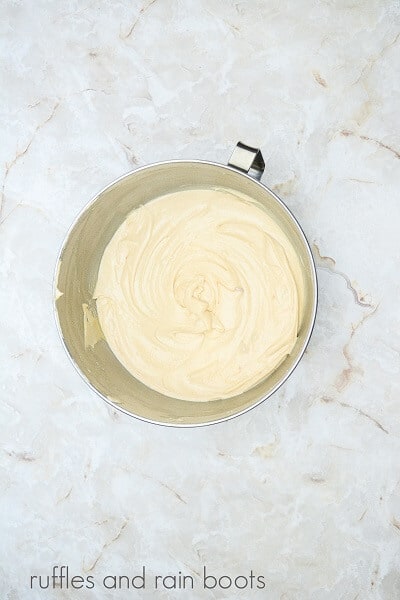 A large metal mixing bowl with cupcake batter inside on a white marble surface.