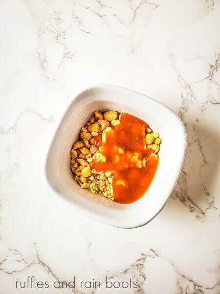 A small white bowl filled with peanuts and caramel sauce against a white marble background.