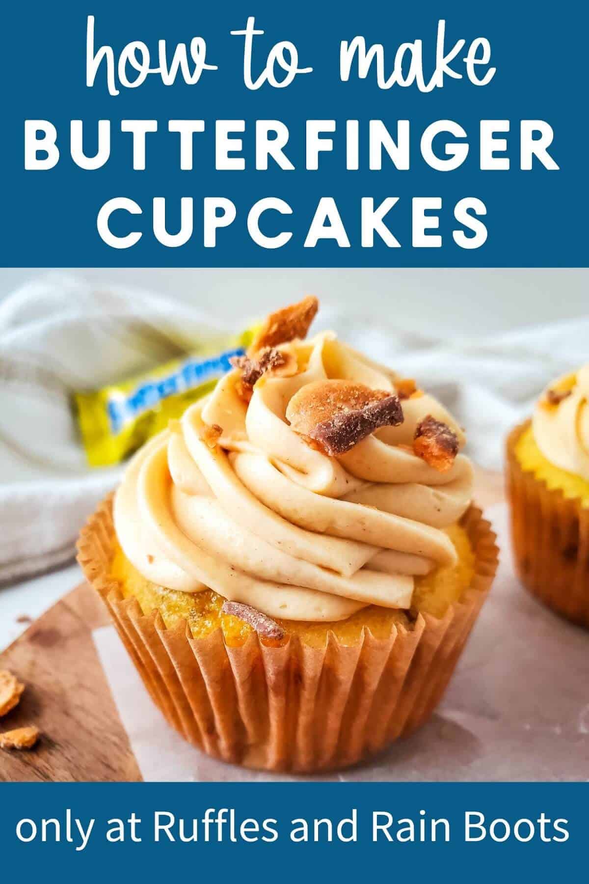 A close up of a Butterfinger cupcake on a wooden surface with a Butterfinger candy bar and a white towel in the background