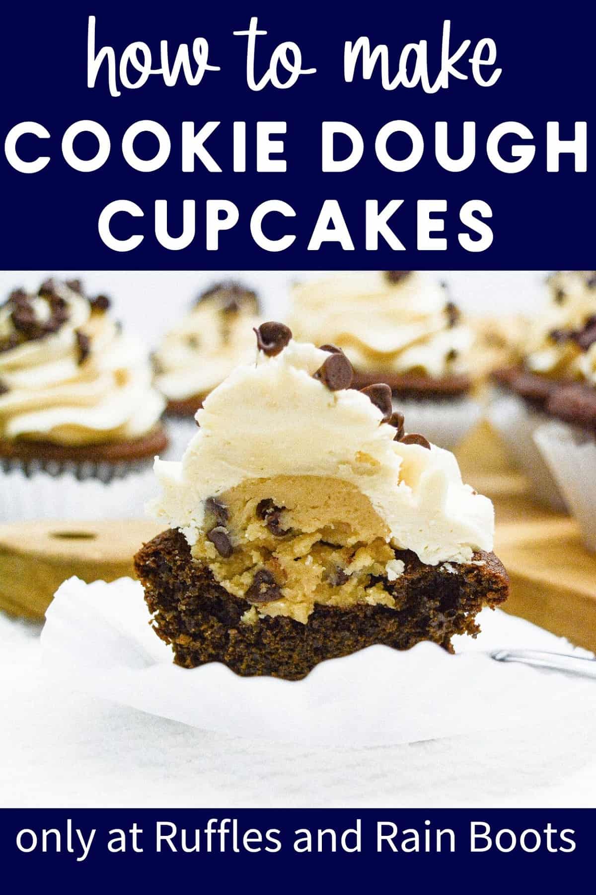 A vertical close up of a frosted cookie dough cupcake that has been cut in half, next to a wooden cutting board, surrounded with more cupcakes.