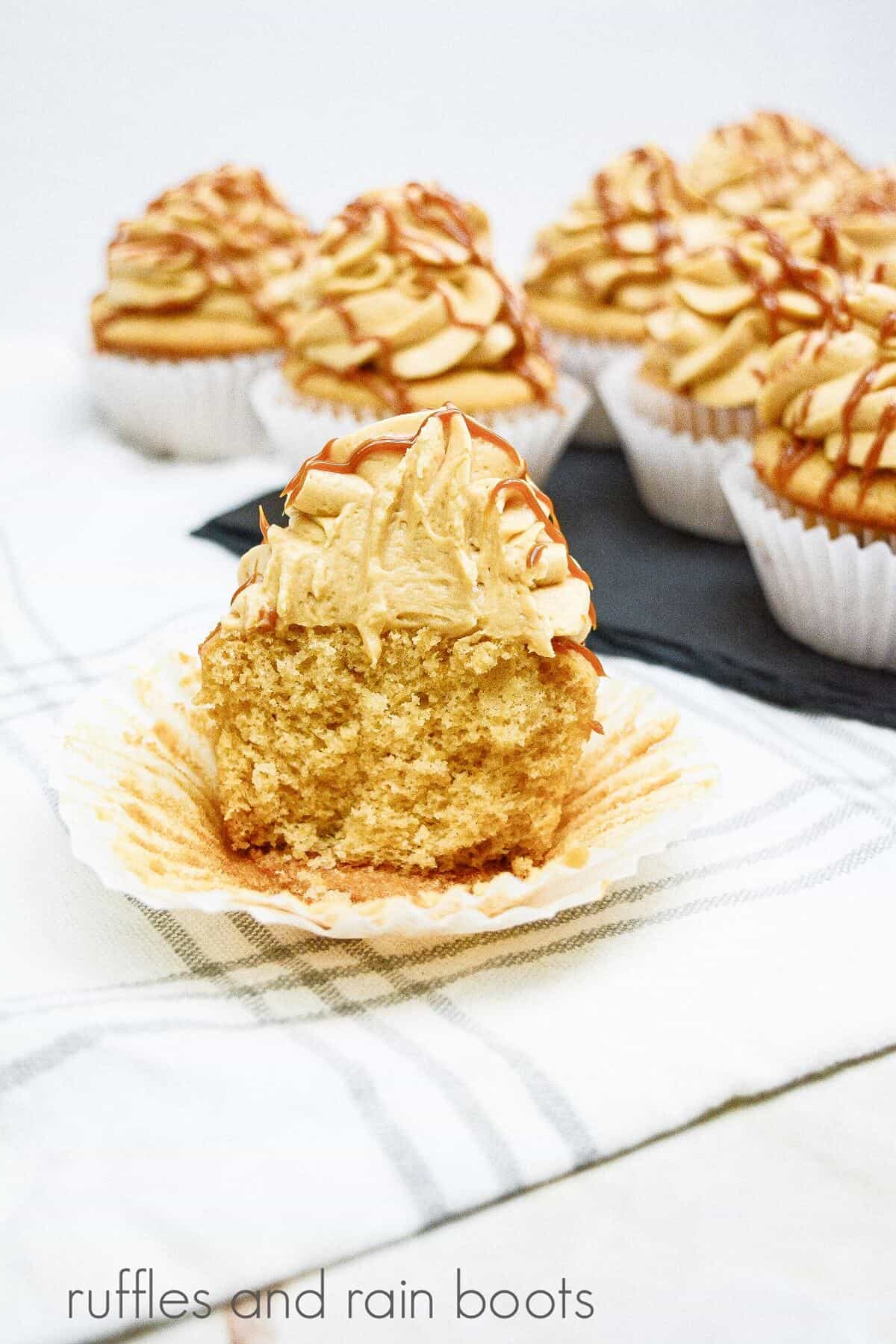 A vertical image of a dule de leche cupcake cut in half with several more cupcakes behind it on a plaid white towel.