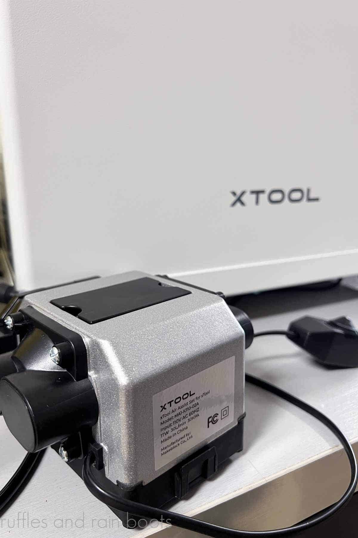Vertical image of the xTool air assist accessory for the M1 laser in front of the smoke purifier on a work bench.