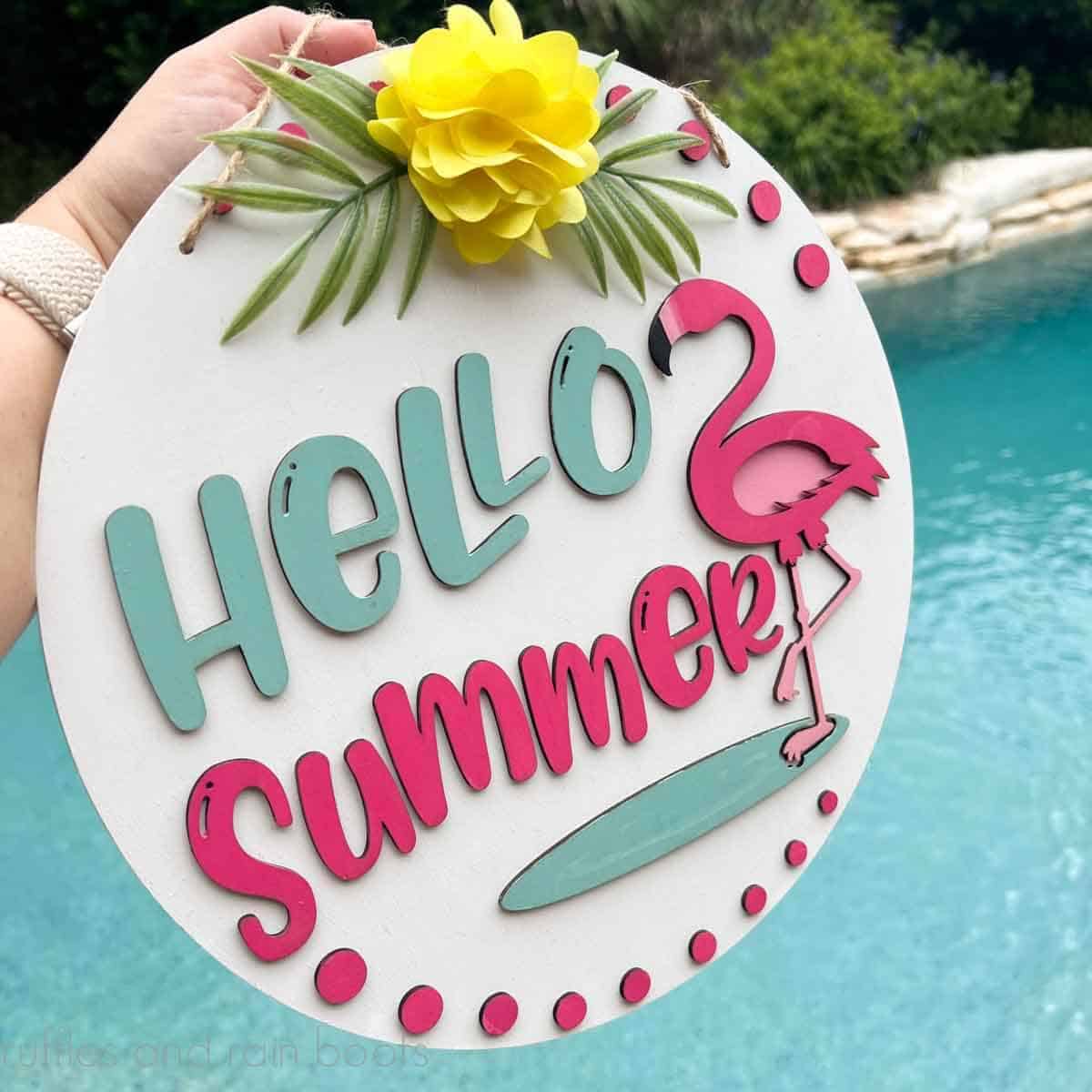Close up square image of a woman holding a hello summer door sign with a flamingo.