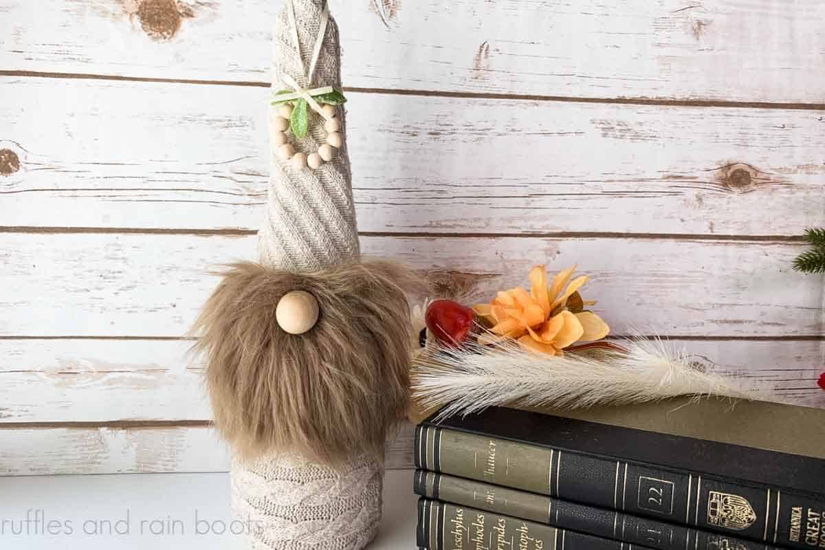 Horizontal image of a wine sleeve gnome made from a thrift store sweater in front of wood background next to books.