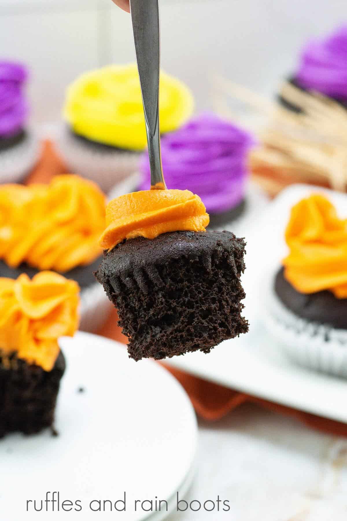 A fork with a bite of the orange frosted Hocus Pocus cupcake with several other cupcakes in the background against a white marble background.
