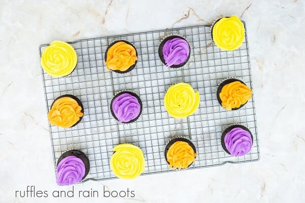 A dozen Hocus Pocus cupcakes on a wire cooling rack against a white marble background.