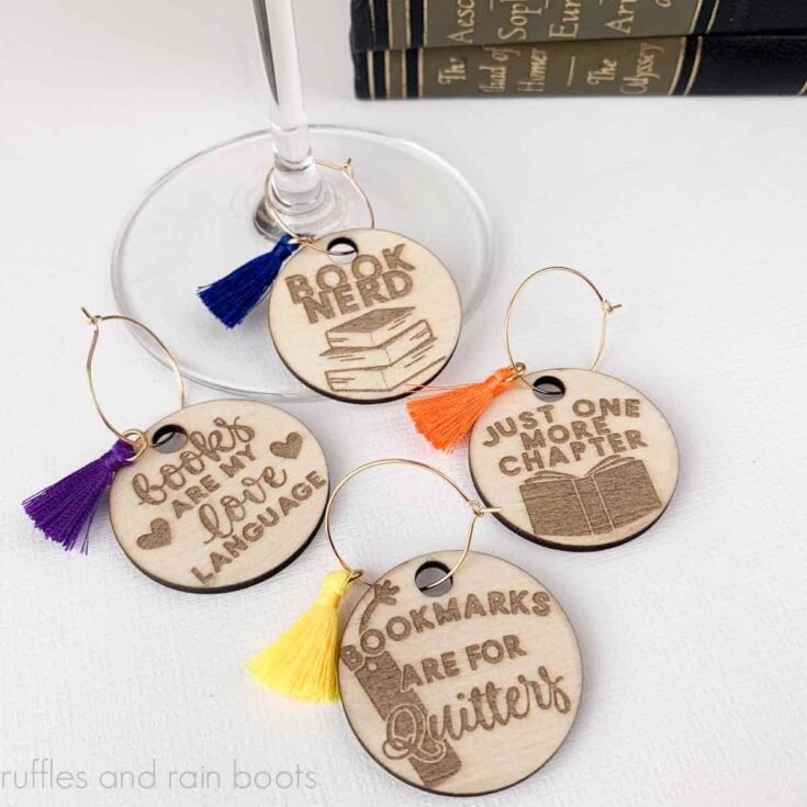 Close up square image of book club themed wood wine charms with colorful tassel on white background.