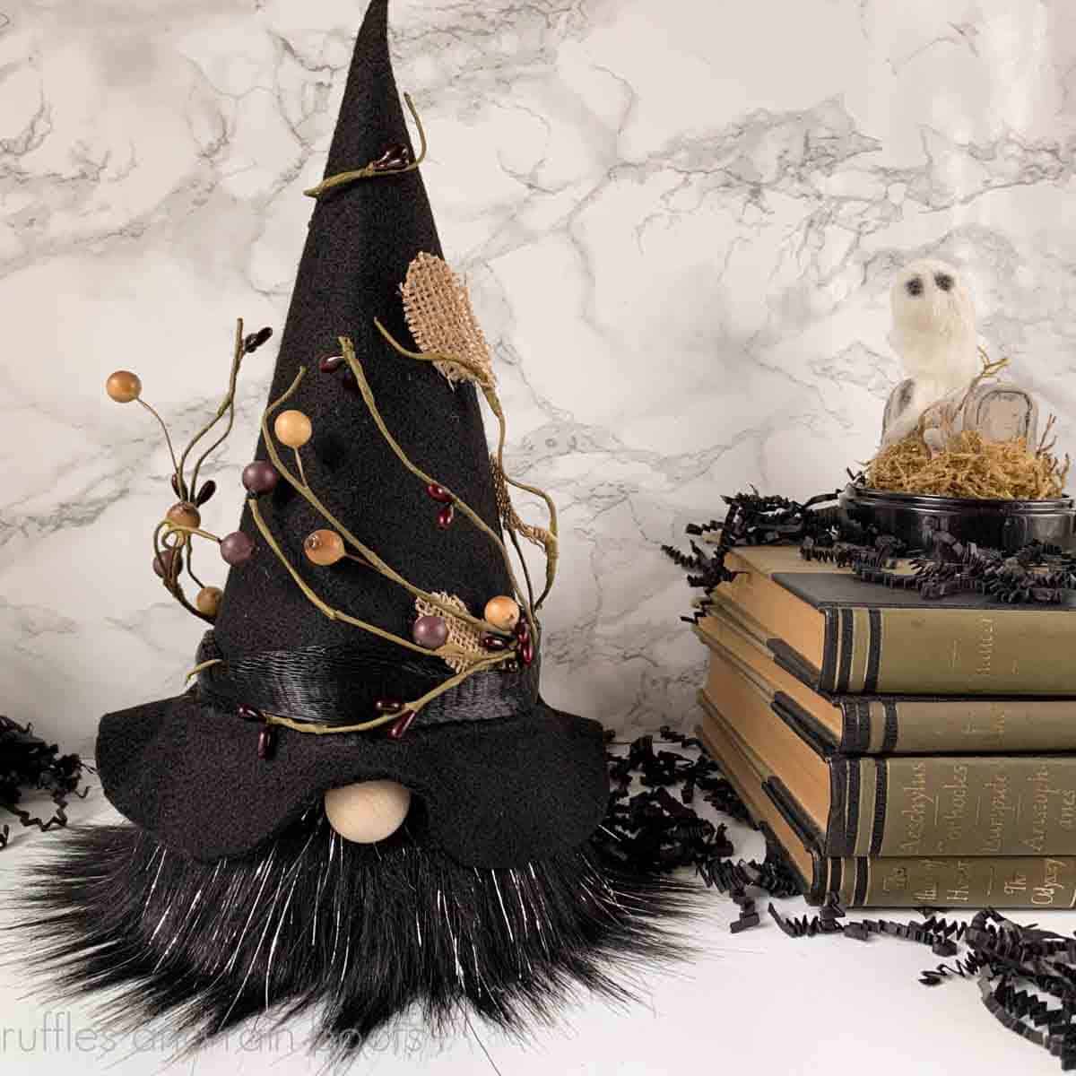 Square image of a witch gnome with black beard, black felt witch hat, and vines on spooky background.