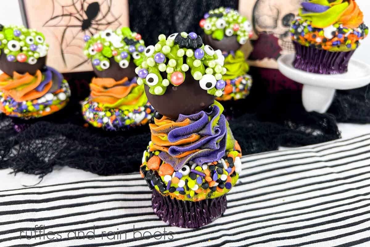 Several cauldron cupcakes on a black cotton netting with Halloween decor with one cupcake in the foreground on a black and white striped towel