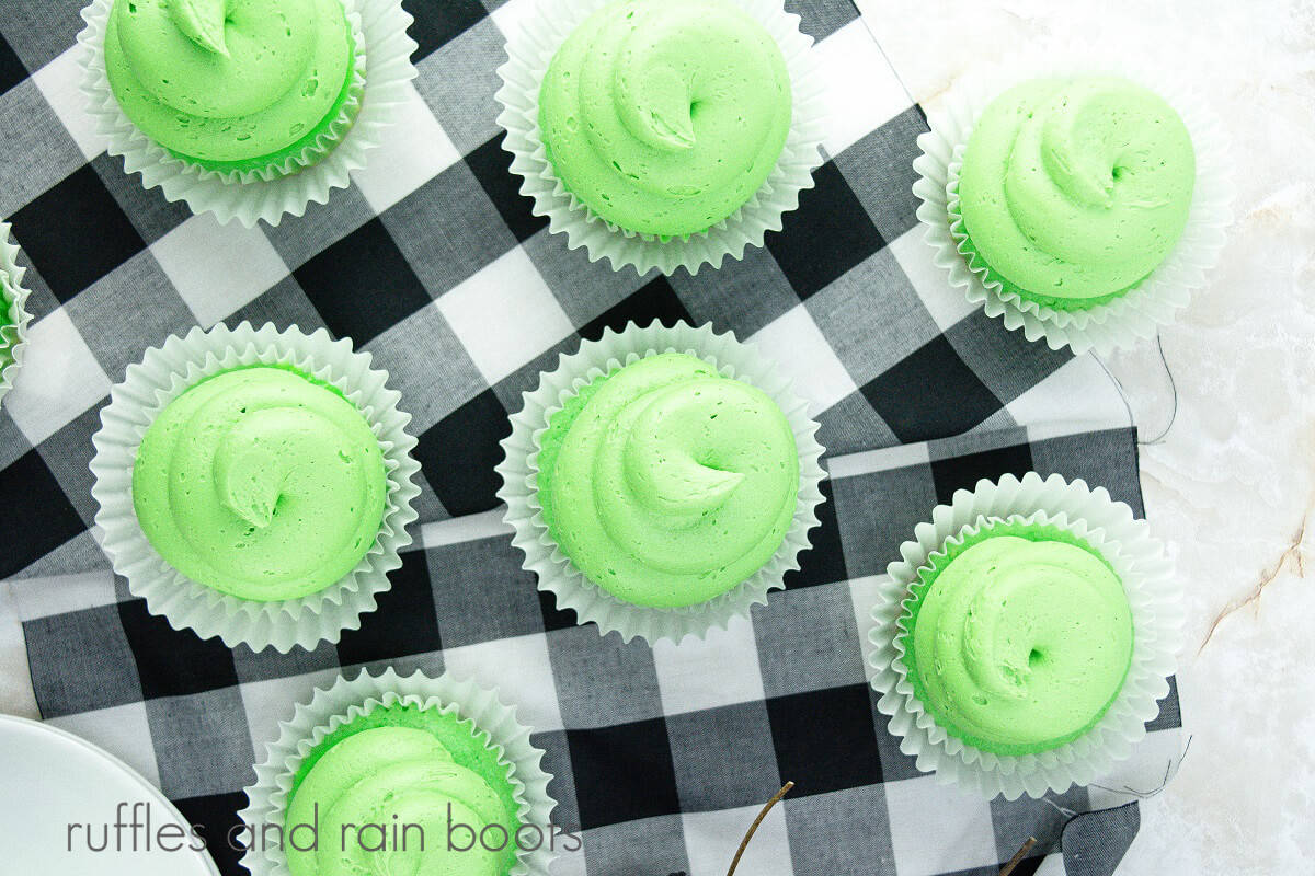 A horizontal image of 7 slime cupcakes on top of a black and white buffalo checked napkin.