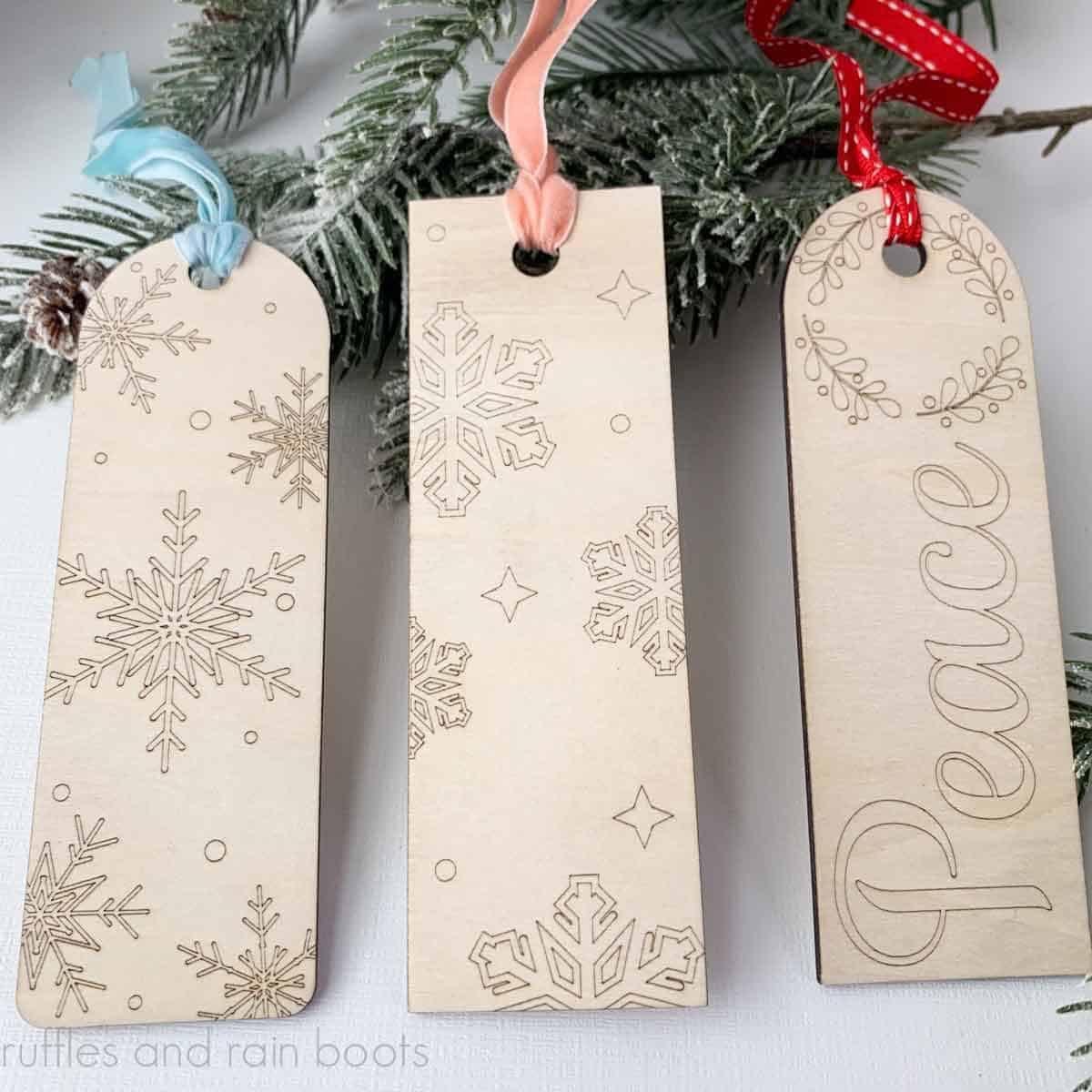 Close up square image of three scored bookmarks with Christmas themes on white background with pine branches.