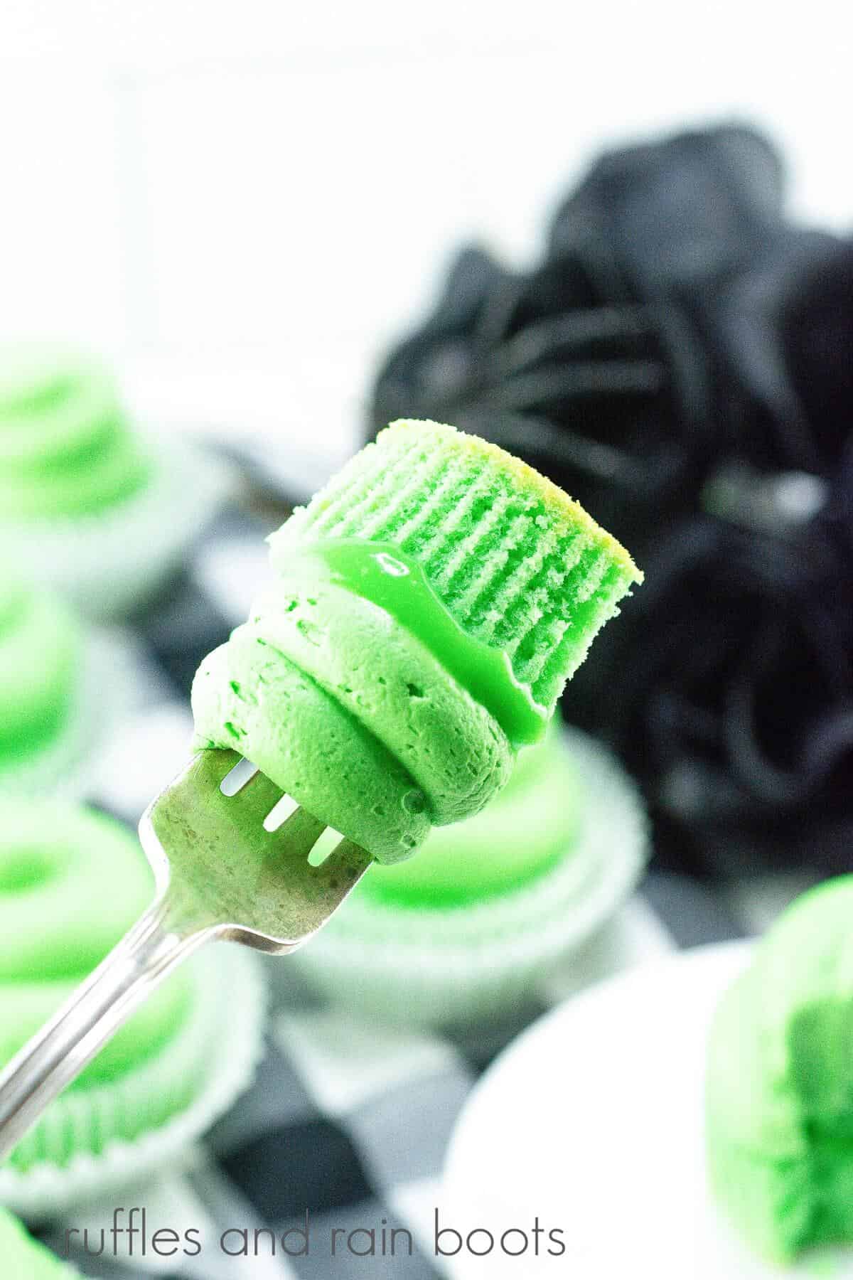 A vertical image of a fork holding a bite of a slime cupcake, against a black and white plaid background and faux black roses.