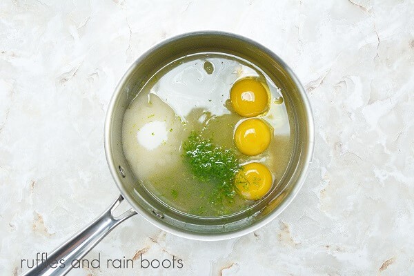 A metal saucepan filled with the ingredients for lime curd against a white marble background.