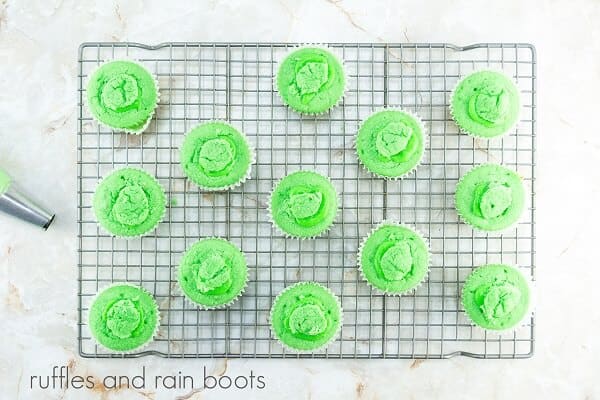 A dozen green slime cupcakes on a metal cooling rack against a white marble background.