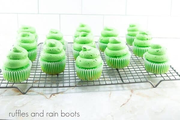 A metal cooling rack filled with green slime cupcakes against a white marble background.
