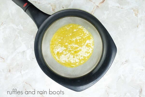 A sieve filled with lime curd against a white marble background.