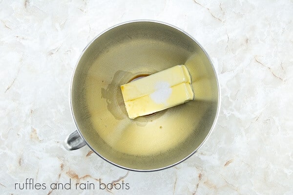 A large metal mixing bowl with butter, vanilla and salt against a white marble background.