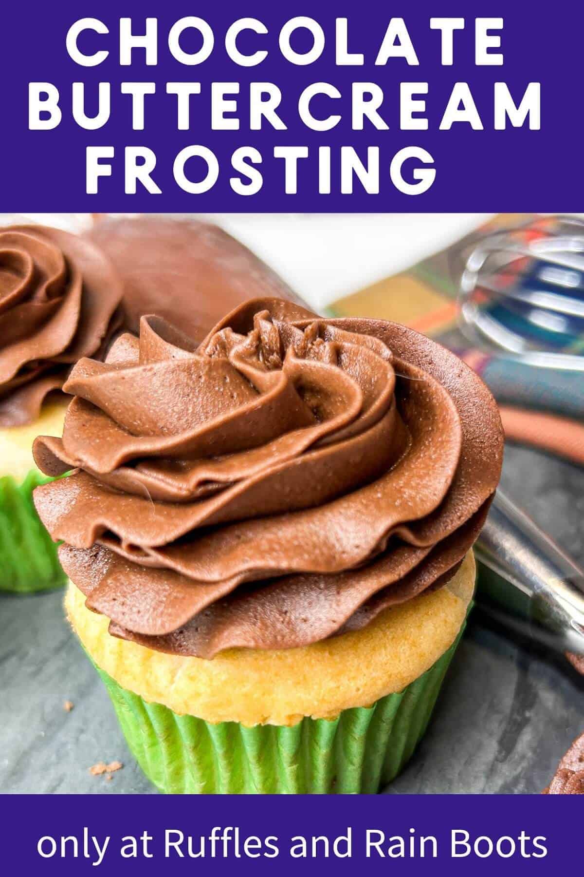 Two frosted cupcakes with chocolate frosting next to a piping bag filled with chocolate frosting on a grey marble slab next to a whisk and a plaid towel against a kitchen backsplash.