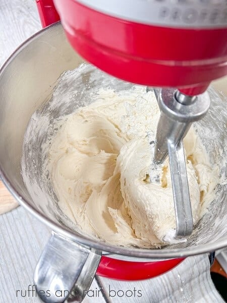 A red stand mixer making marshmallow buttercream frosting in a large metal mixing bowl with a paddle attachment.
