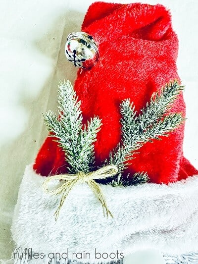 A Santa hat with a pine pick and a twine bow against a white background.