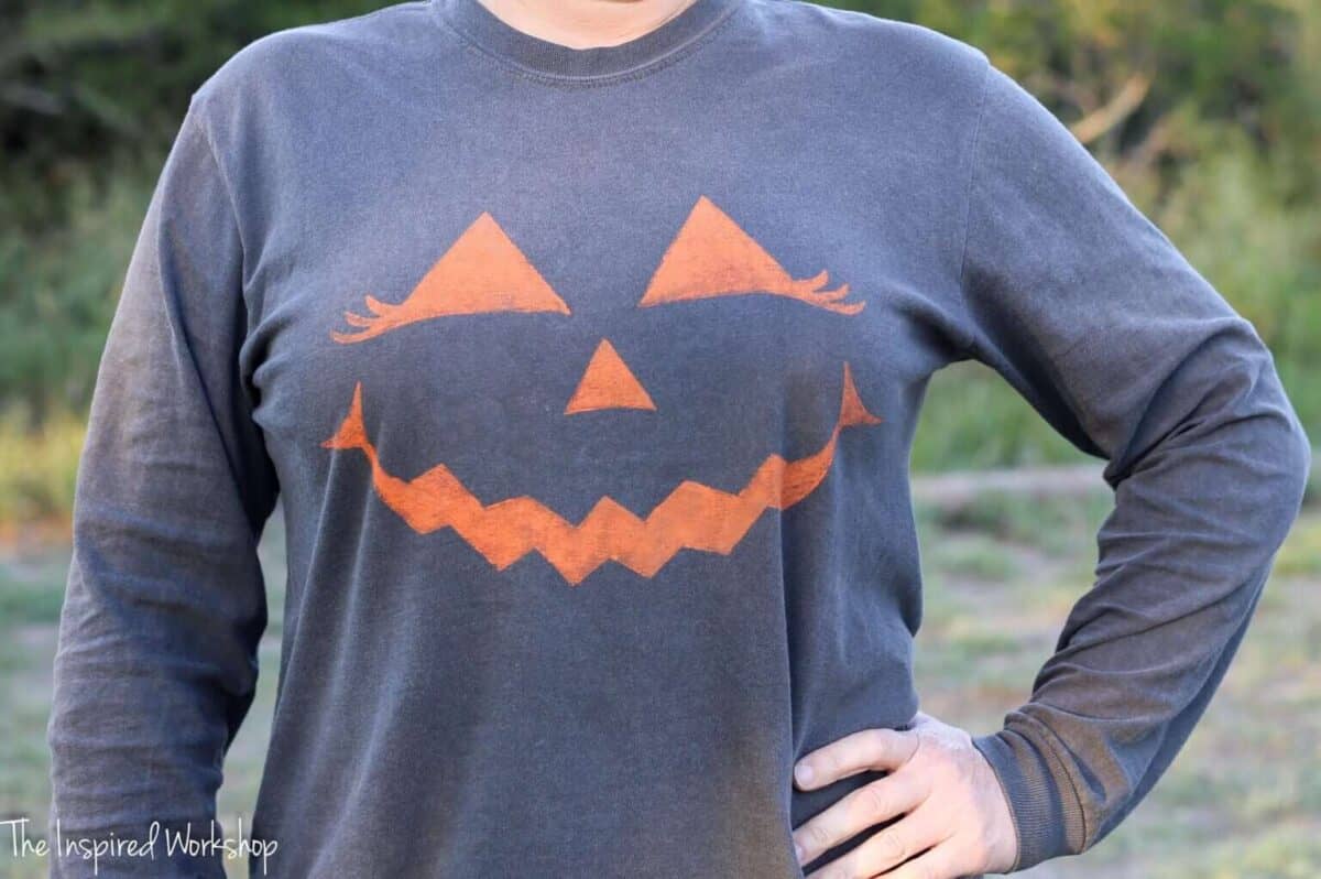 Horizontal image of woman in dark t-shirt with orange painted, happy Jack O Lantern.