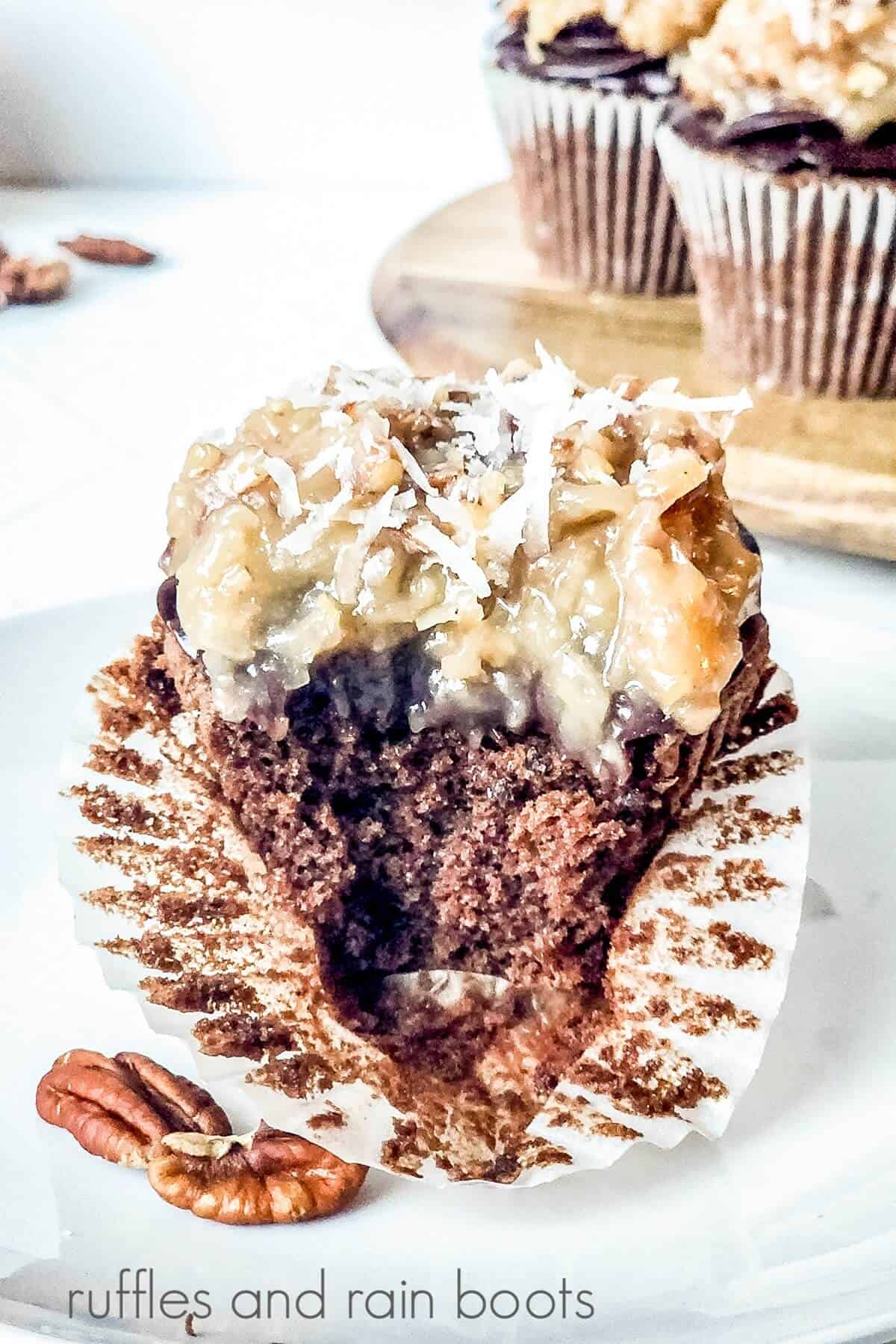 A German cupcake with a bite taken out of it with a wooden cutting board filled with more cupcakes against a white surface.