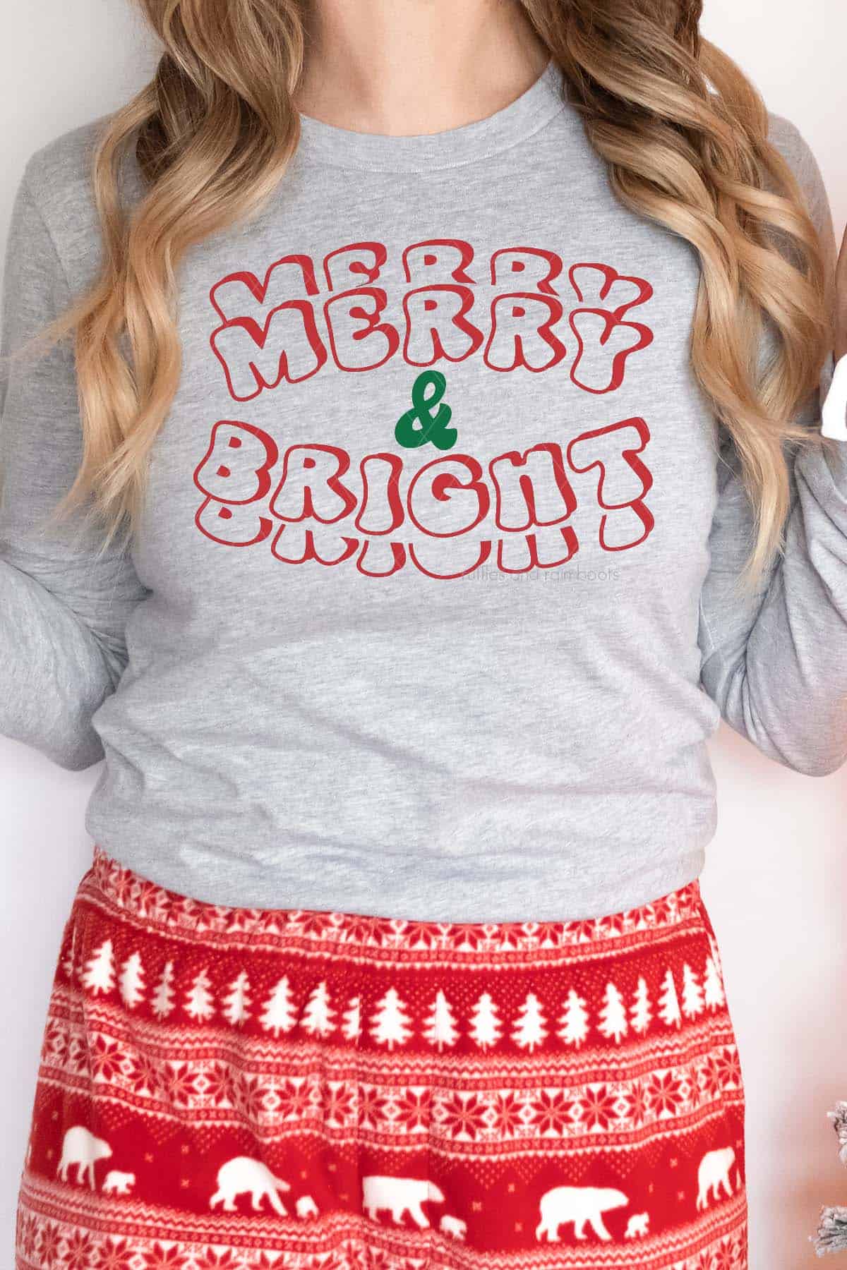 Vertical image of woman in Nordic pajama bottoms and grey long sleeve shirt which reads merry and bright in red and green heat transfer vinyl.