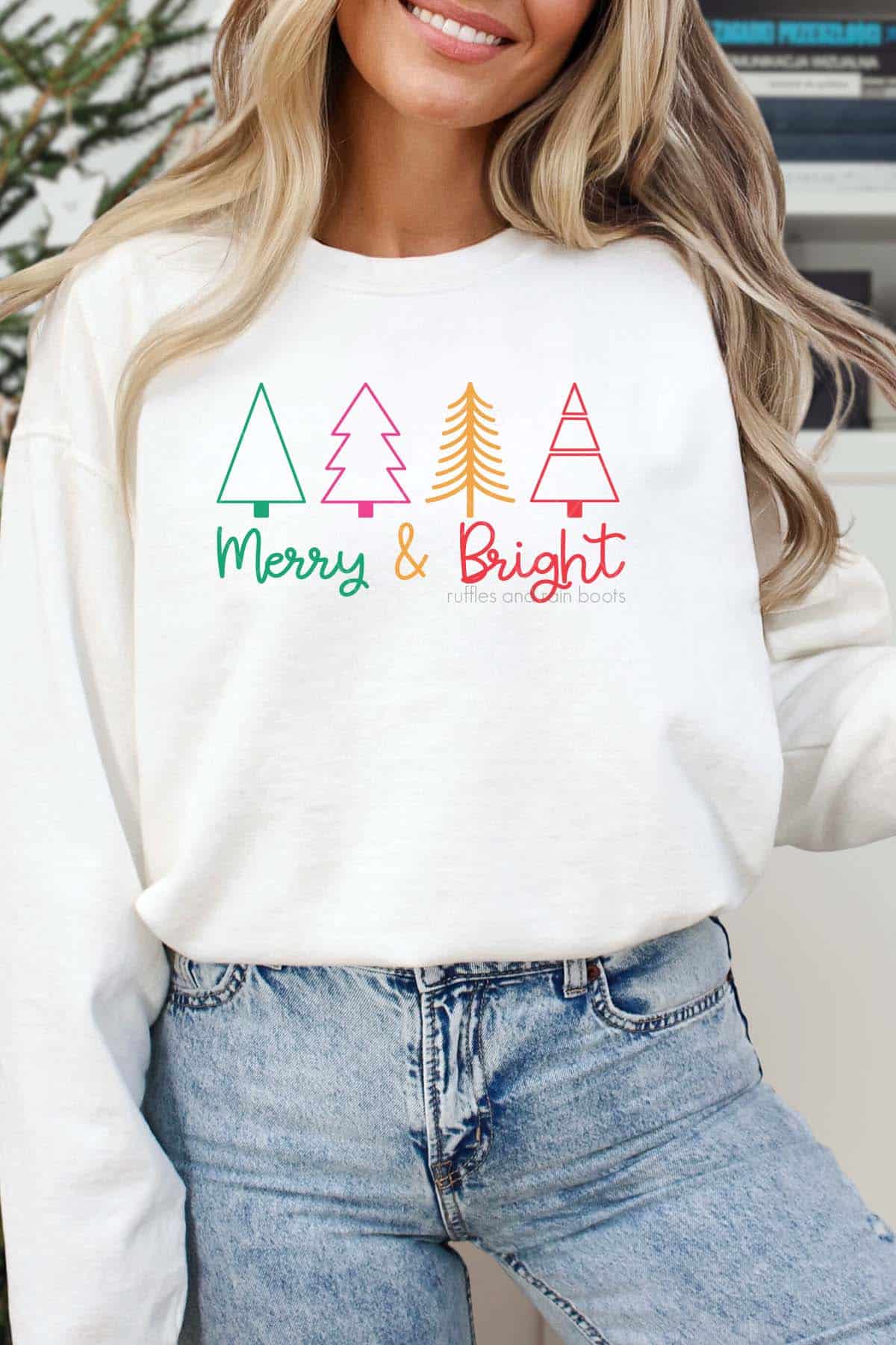 Vertical image of woman in front of holiday background wearing white shirt with trees and merry and bright in bold colors.