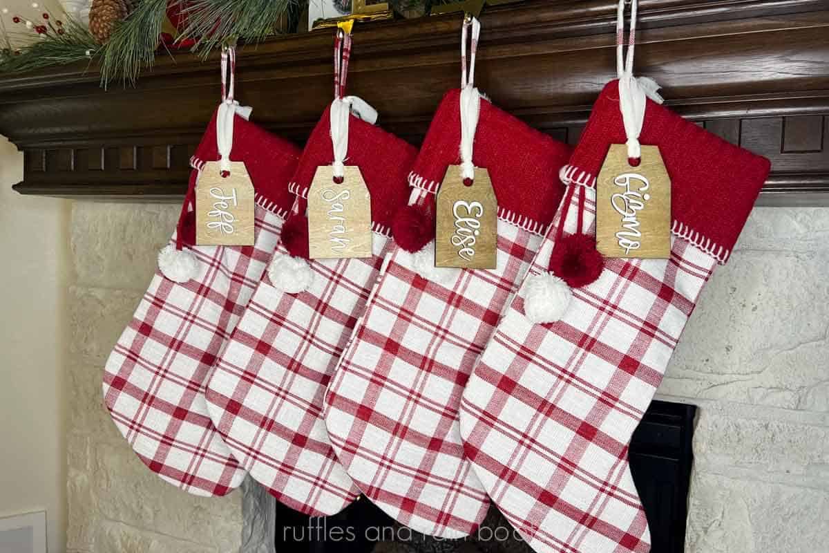 Horizontal image of four red stockings hung on a wood mantel, each with a wooden stocking tag with a name on it.