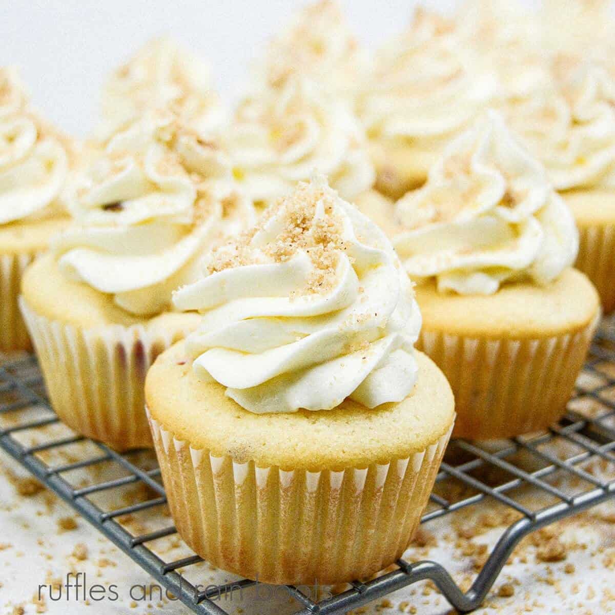 A metal cooling rack filled with a dozen peach streusel cupcakes against a white marble background.