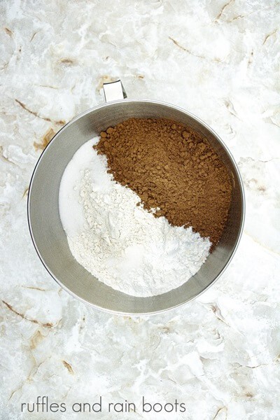 A large metal mixing bowl with the dry ingredients against a white marble background.