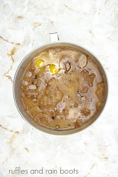 A large metal mixing bowl with the ingredients for the batter against a white marble background.