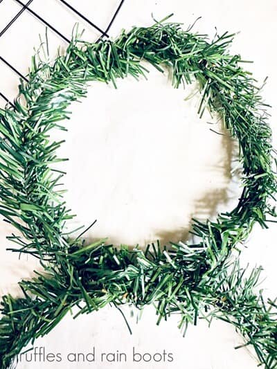 A Dollar Tree snowman wreath, wrapped in faux green garland, against a white background.