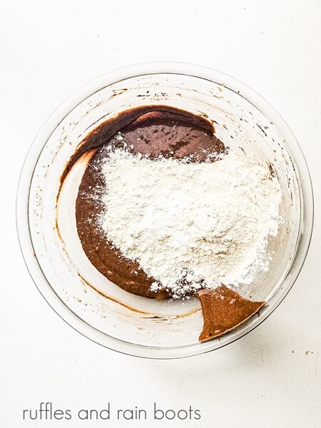 The wet ingredients for German chocolate cupcakes with the dry ingredients on top against a white surface.