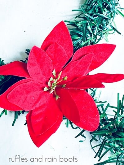 A red poinsettia glued onto a snowman wreath against a white background.