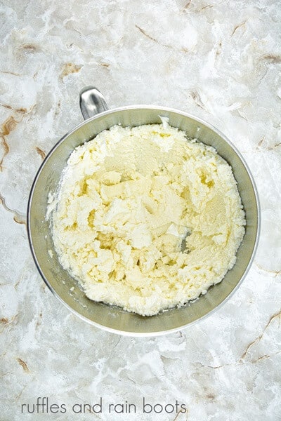 A large metal mixing bowl filled with frosting against a white marble background.