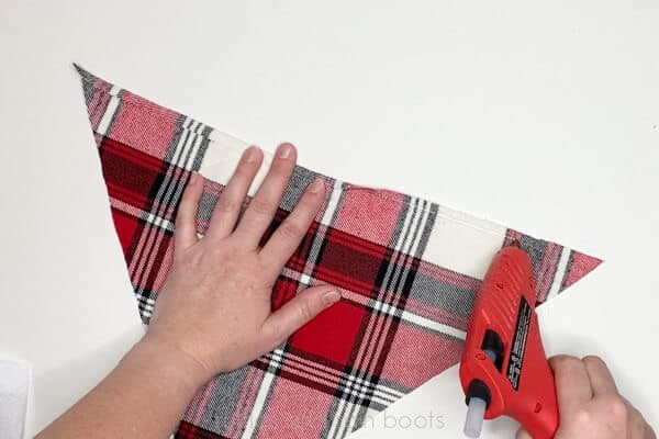 Horizontal image of a crafter using a red glue gun to add a small brim to a red flannel gnome hat.