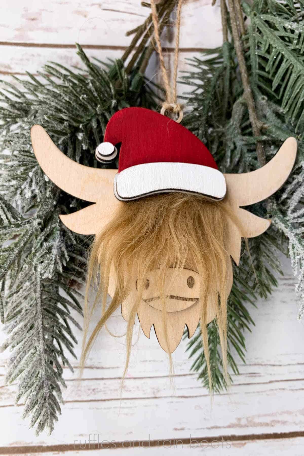 Vertical close up image of a highland cow in a Santa hat with a faux fur accent.