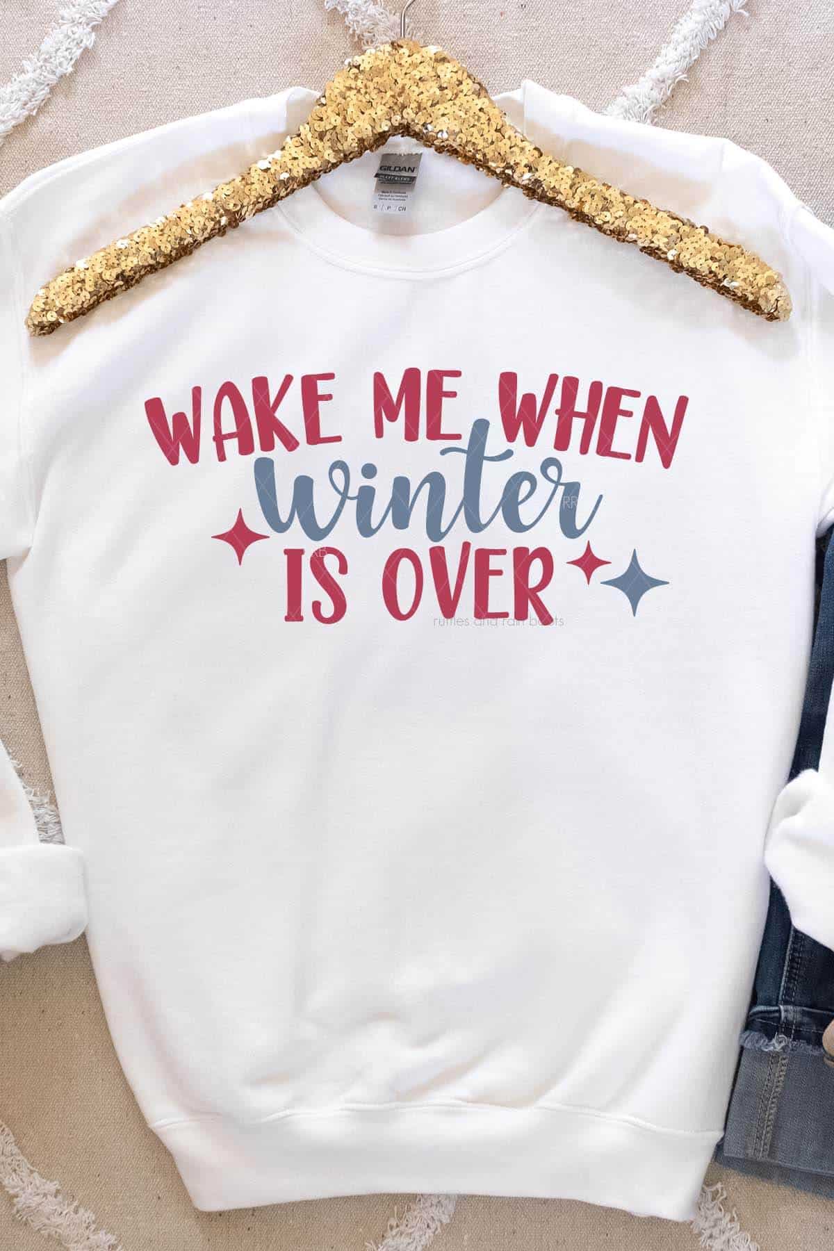 Vertical image of a gold hanger and white sweatshirt which reads wake me when winter is over in red and blue heat transfer vinyl.