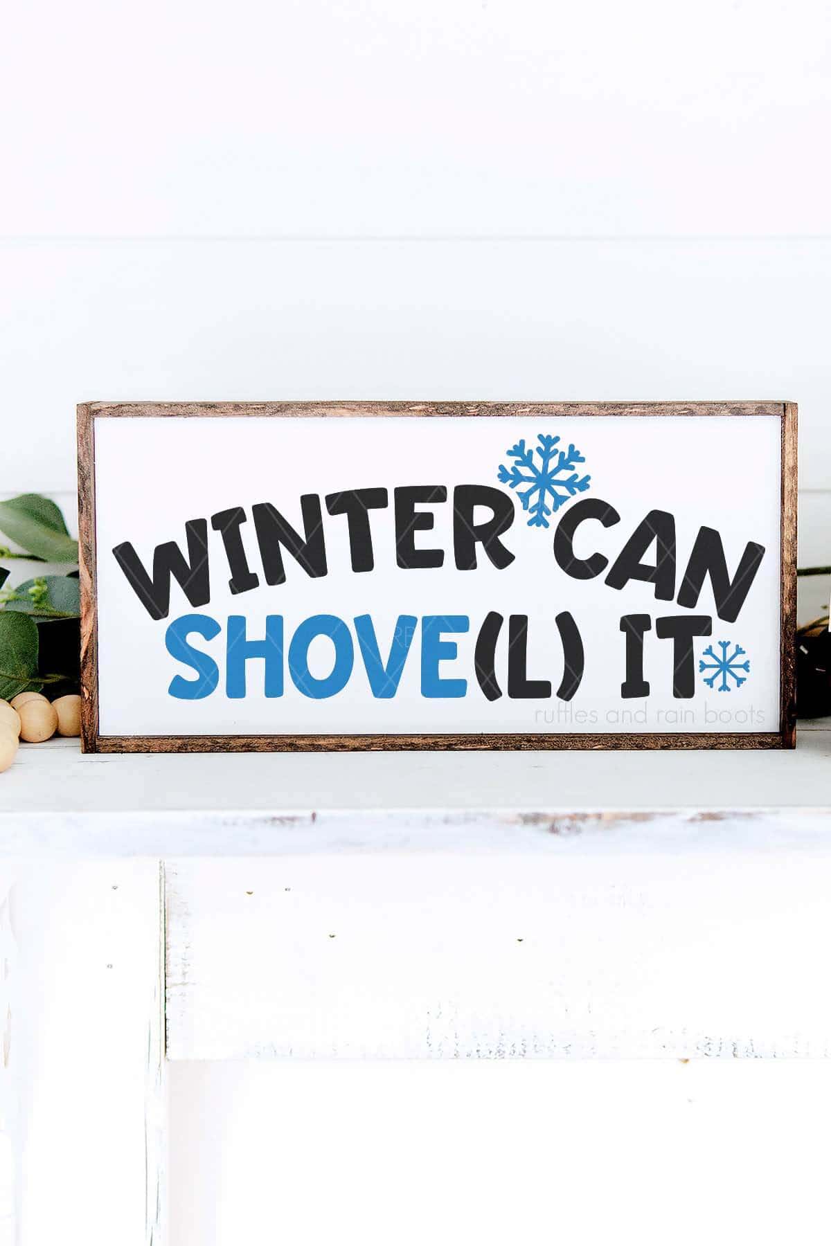 Vertical image of a horizontal, white sign on a mantle with greenery which reads Winter Can Shovel It.