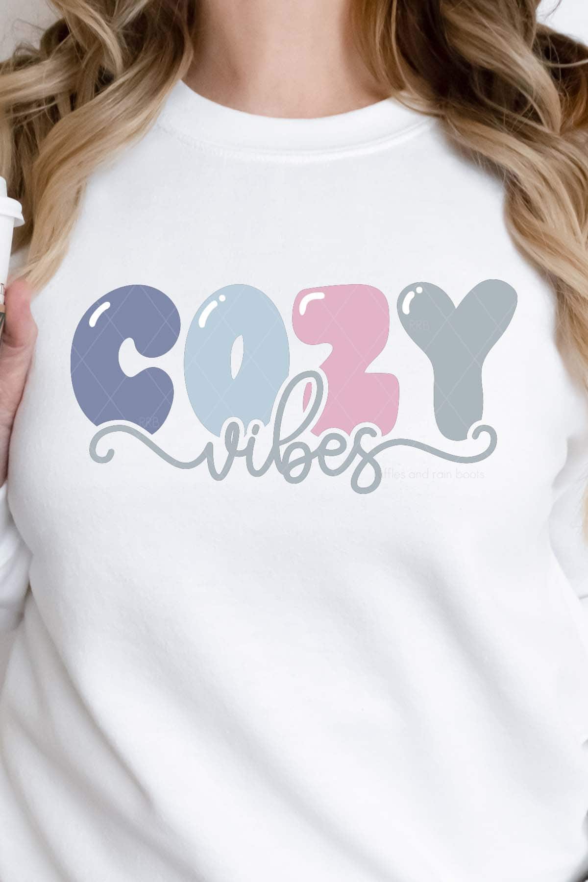 Vertical image of woman in white sweatshirt which reads cozy vibes in pastel colored heat transfer vinyl.