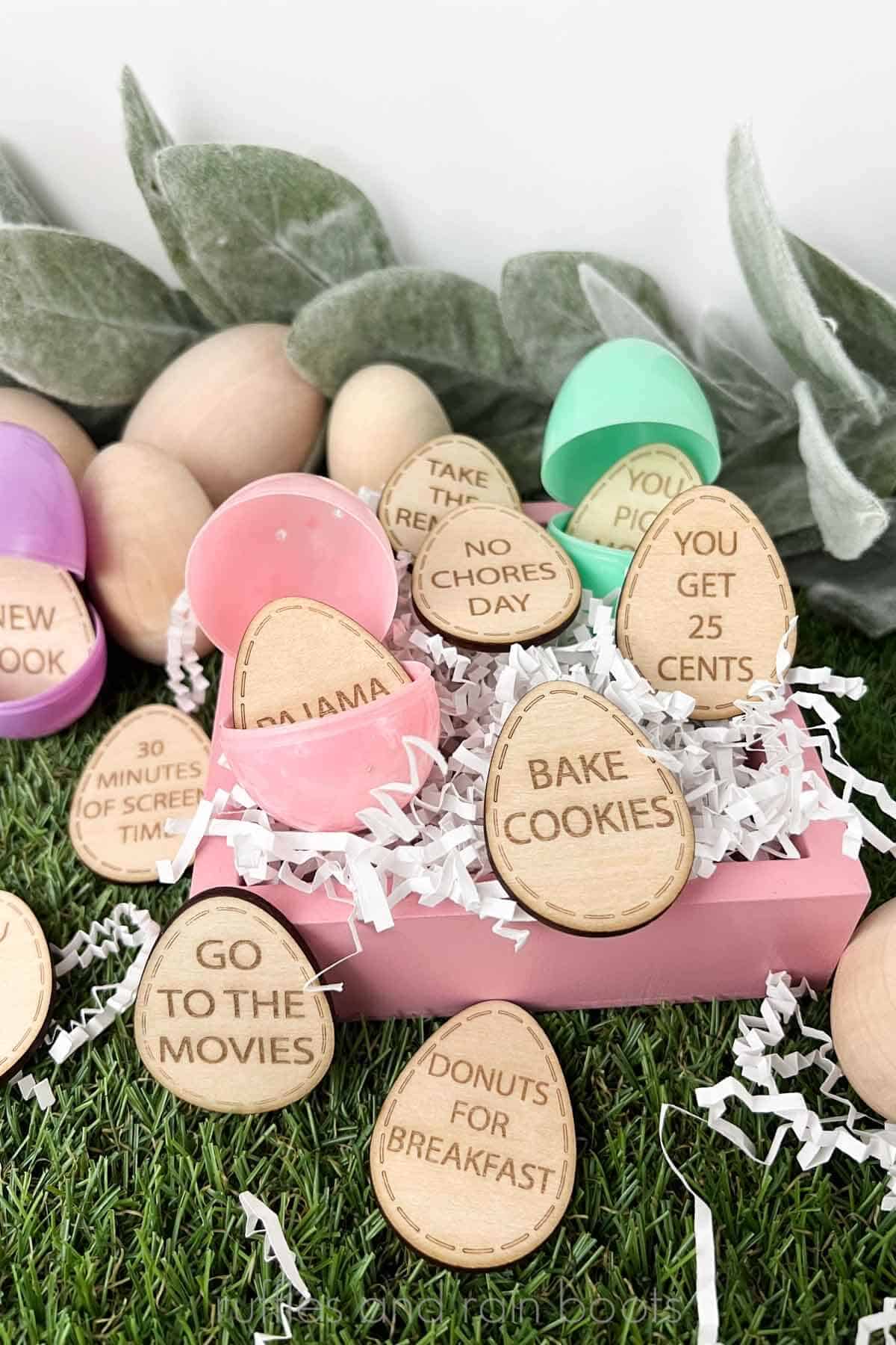 Vertical image of wooden Easter egg tokens placed in plastic eggs in a pink frame with white paper shreds.