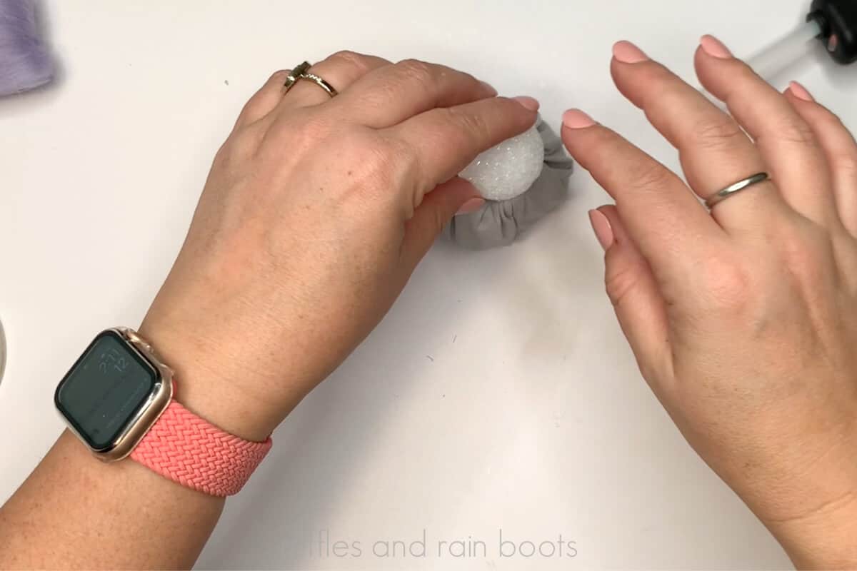 Horizontal image of a crafter gluing a foam ball to a fabric covered jar.