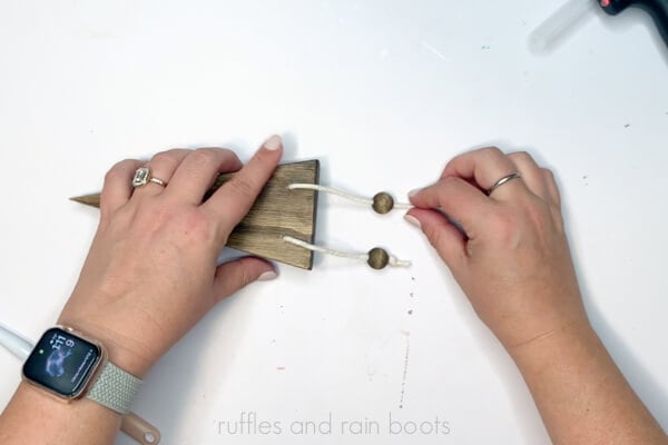 Horizontal image of a crafter tying wood beads onto macrame cords to form gnome legs.